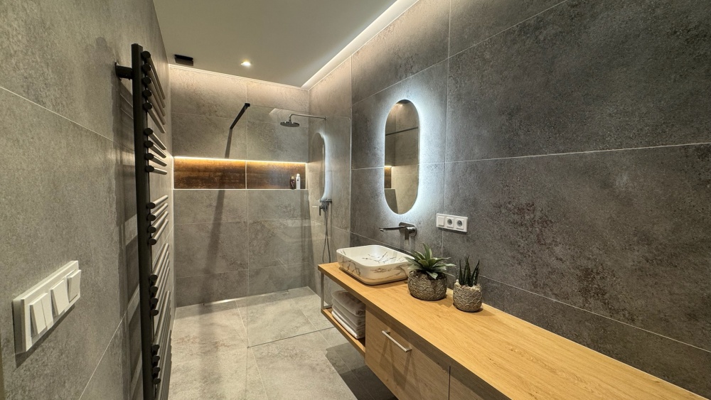 mramorové umyvadlo, dřevěné skříňky, kamenné kachličky, oválné zrcadlo 